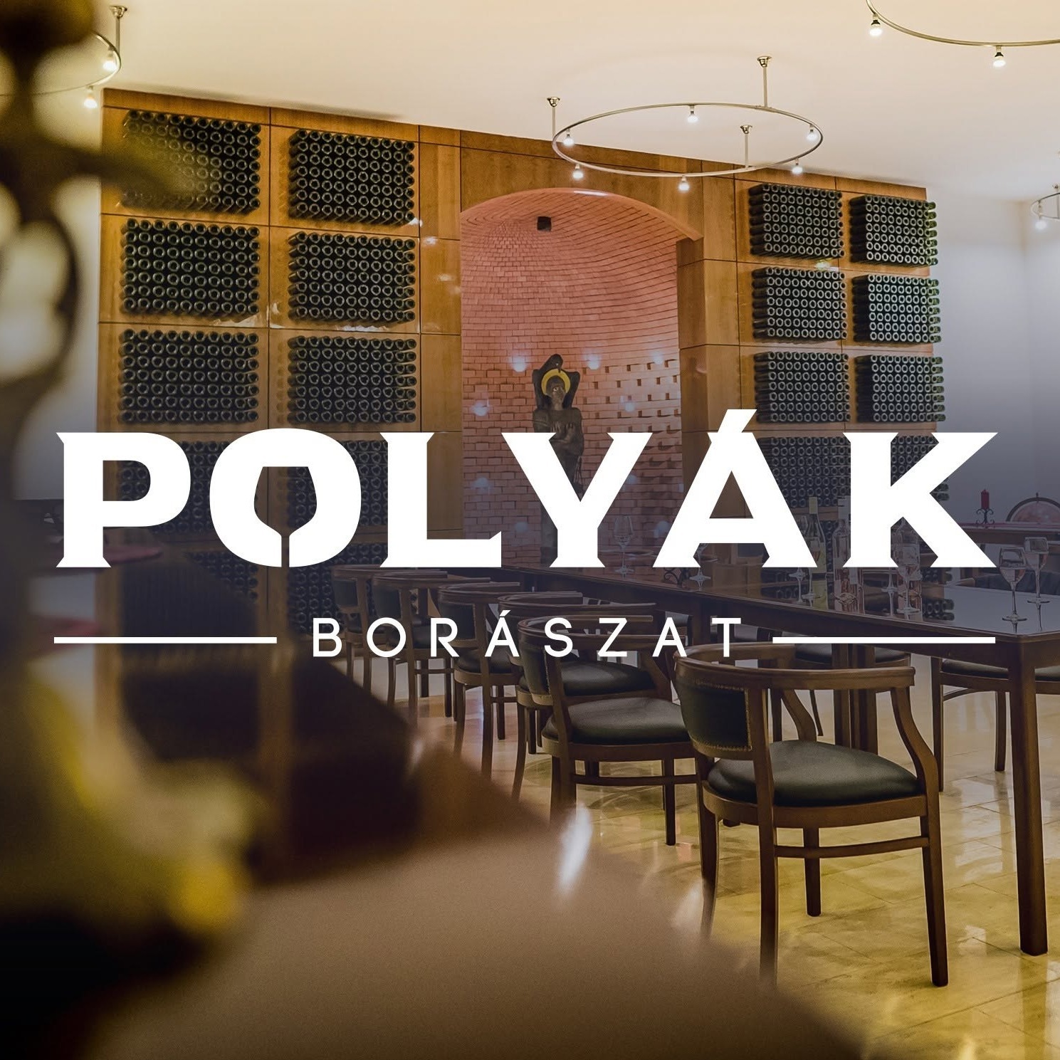 A képen Polyák Borászat felirat, háttérben székek és asztalok egy teremben.