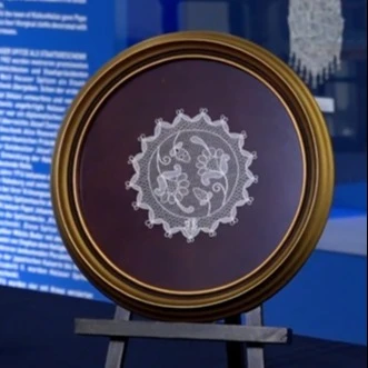 A képen egy állványon halasi csipke kiállított darabja látható.