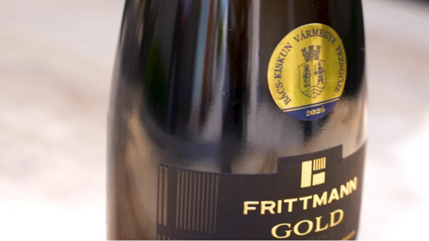 A képen egy palack Frittmann Gold pezsgő üvege látható, rajta a Bács-Kiskun vármegye bora matricával.