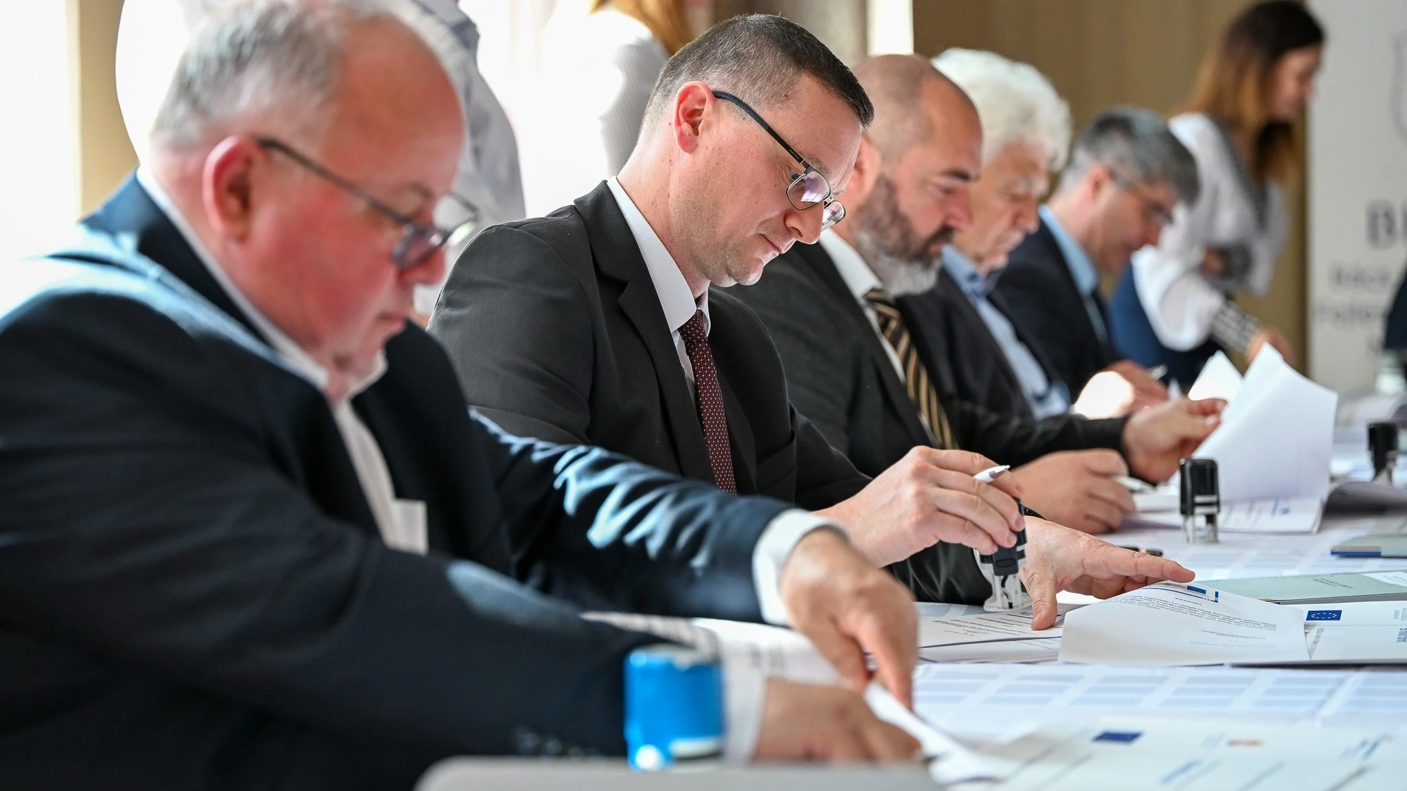 A képen 5 úriember szerződéseket ír alá.